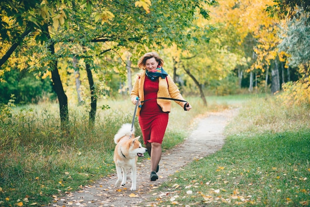 Mädchen mit dem niedlichen jungen foxy Hund läuft entlang Weg unter Herbstlaub im Herbstpark