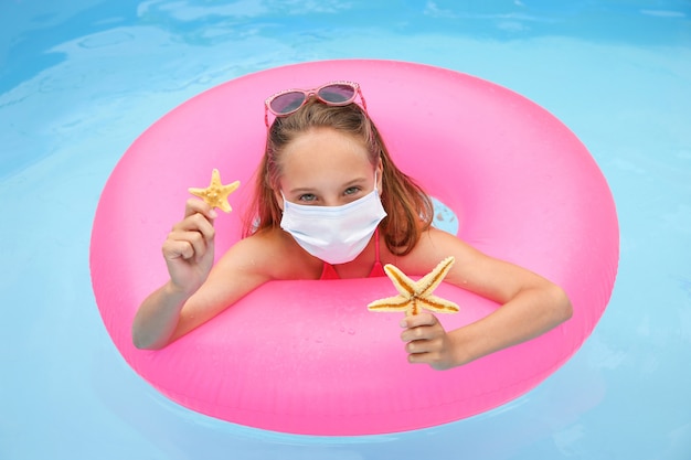 Mädchen mit der medizinischen Maske auf ihrem Gesicht im Pool.