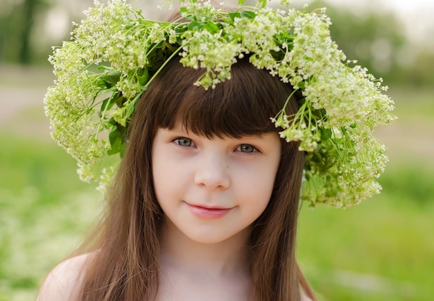 Mädchen mit dunklen langen Haaren und grünen Augen mit einem Blumenkranz auf dem Kopf