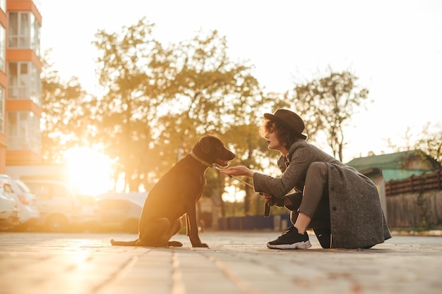 Mädchen mit einem Hund, der bei Sonnenuntergang auf der Straße im Hintergrund der Stadt sitzt