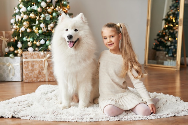 Mädchen mit einem Hund nahe dem Weihnachtsbaum auf dem Weihnachtshintergrund