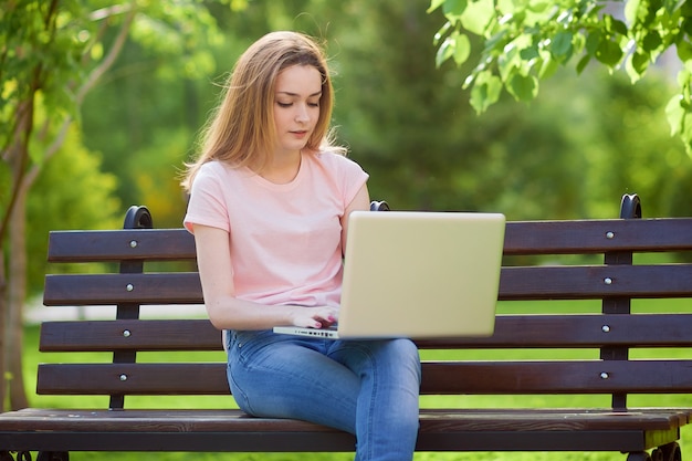 Mädchen mit einem Laptop, der auf einer Bank im Park sitzt