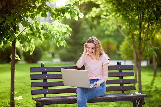 Mädchen mit einem Laptop, der auf einer Bank im Park sitzt