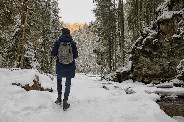 Mädchen mit einem Rucksack steht einen schneebedeckten Wald.