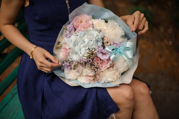 Mädchen mit einem schönen Blumenstrauß der pastellfarbenen Blumen auf der Bank