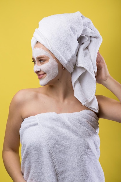 Mädchen mit einer kosmetischen Maske im Gesicht in einem weißen Handtuch.