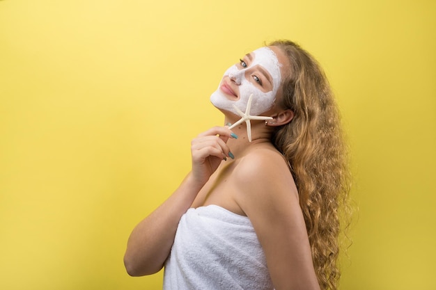 Mädchen mit einer kosmetischen Maske im Gesicht in einem weißen Handtuch.