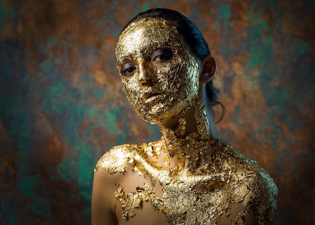 Mädchen mit einer Maske auf ihrem Gesicht aus Blattgold Düsteres Studioporträt einer Brünette auf abstraktem Hintergrund