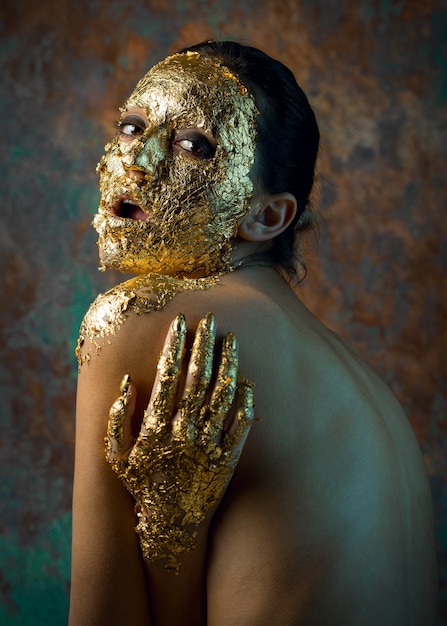 Mädchen mit einer Maske im Gesicht aus Blattgold Düsteres Studioporträt einer Brünetten