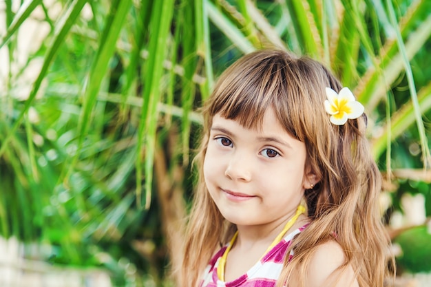Mädchen mit einer Plumeriablume in ihrem Haar gegen den Hintergrund von Palmen. Selektiver Fokus