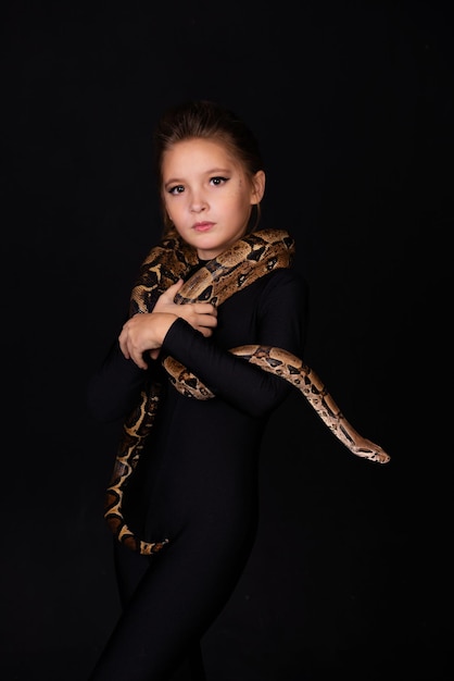 Mädchen mit einer Schlange am Körper auf schwarzem Hintergrund