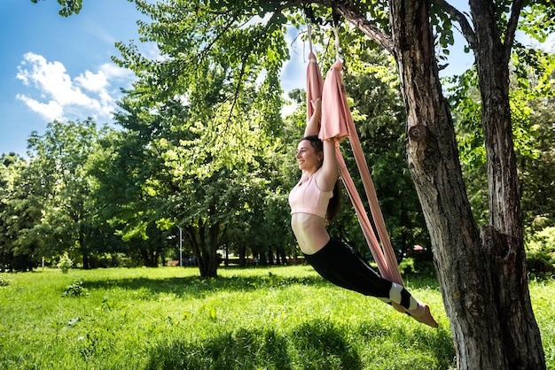 Mädchen mit einer schönen gepumpten Figur in einem Sportanzug für Yoga erstreckt sich in der Luft in der Nähe eines Baumes Das Konzept der Luftbilder im Freien