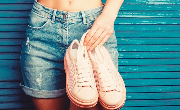 Mädchen mit einer schönen Taille in Jeansshorts Frau, die ein Paar rosa Schuhe hält