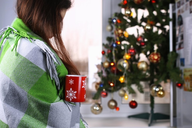 Mädchen mit einer Tasse Heißgetränk steht in der Silvesternacht vor einem Fenster