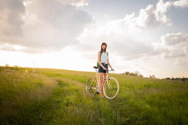 Mädchen mit Fahrrad in der schönen ländlichen Gegend. Junge hübsche weibliche Person mit Retro-Fahrrad, das in einer Wiese am hellen sonnigen Nachmittag im Sommer steht
