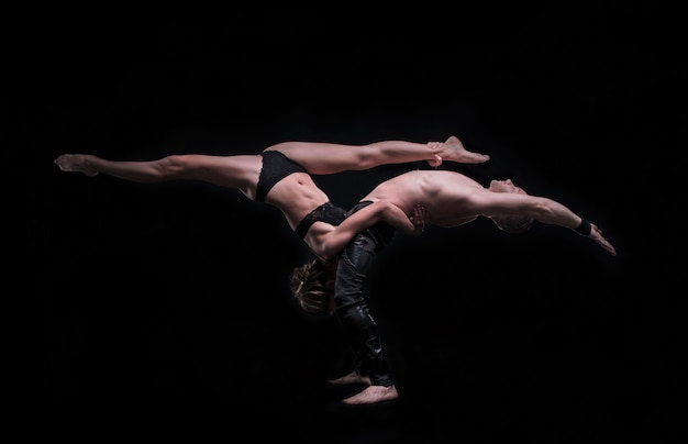 Mädchen mit Freund führen schöne Gymnastikelemente durch. schönes akrobatisches paar. schwarzer Hintergrund