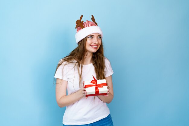 Mädchen mit Geschenk in der Hand und Hirschhörnern auf blauem Hintergrund lächelt vor Freude und Glück zu Weihnachten...