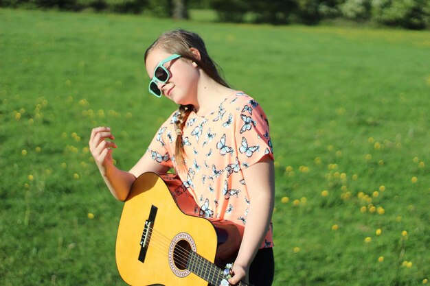 Foto mädchen mit gitarre, das an einem sonnigen tag auf einem grasbewachsenen feld steht