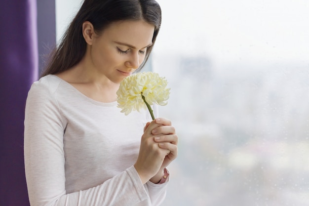 Mädchen mit großer hellgelber Blume nahe dem Fenster