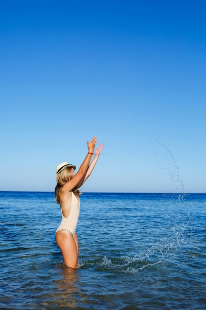 Mädchen mit hellem Hut und beigem Badeanzug spritzt im blauen Wasser des Roten Meeres