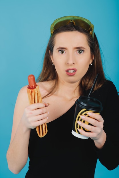 Mädchen mit Hotdog und Glas mit Kaffee auf blauem Hintergrund