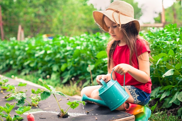 Mädchen mit Hut bewässert Pflanzen im Garten