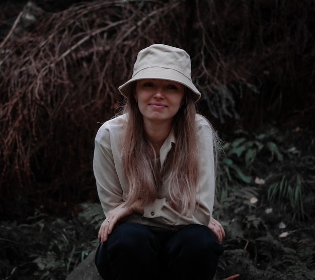 Foto mädchen mit hut sitzt und lächelt im wald