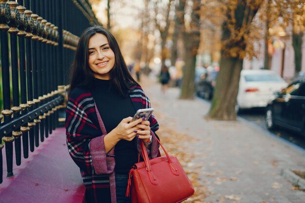 Mädchen mit ihrem Handy während des Gehens durch den Park im Herbst