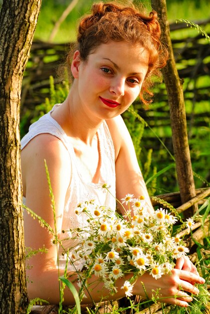 Mädchen mit Kamille Haufen stehen ordentlich den Holzzaun. Ländliches Porträt.