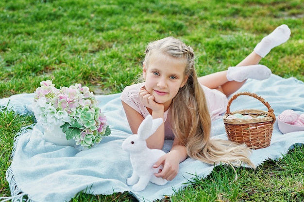 Mädchen mit Kaninchen und Eiern für Ostern im Park auf grünem Gras