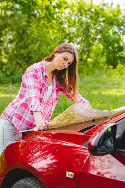 Mädchen mit Karte in der Hand, die neben einem Auto im Wald steht