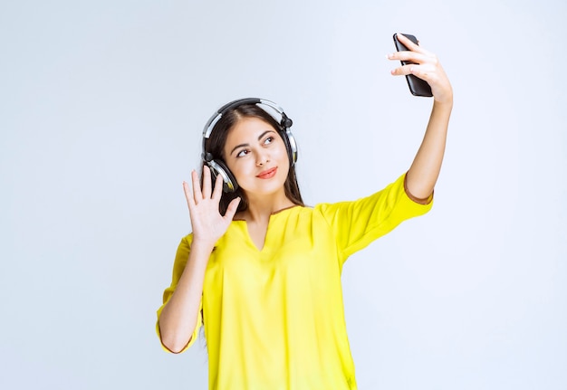 Mädchen mit Kopfhörern, die ihr Selfie machen oder einen Videoanruf tätigen.