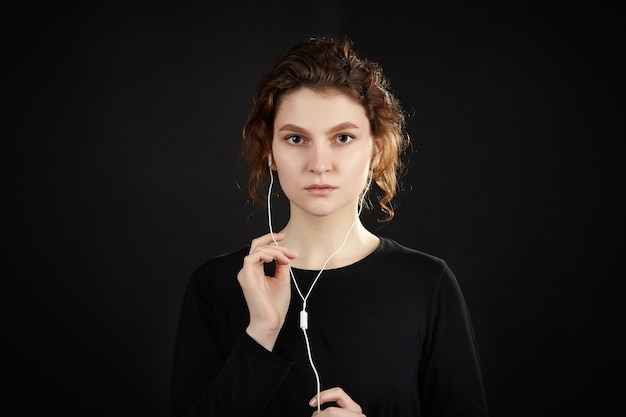 Mädchen mit Kopfhörern hört Musik. Nahaufnahmeportrait vor einem schwarzen Hintergrund.