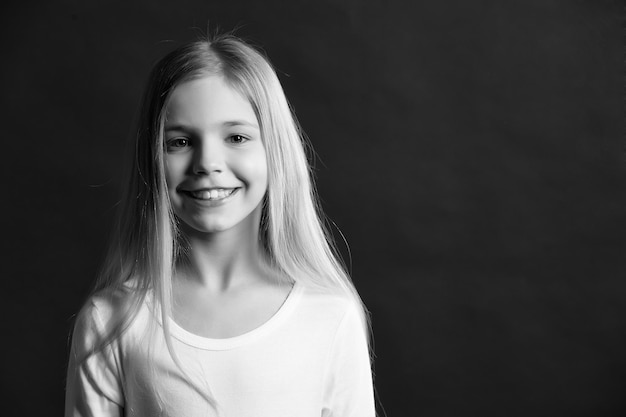 Mädchen mit Lächeln auf süßem Gesicht auf dunklem Hintergrund Kindermodell lächelt mit langem, gesundem Haar Glückliches Kind-Kindheits-Konzept Beauty-Look-Frisur Jugend-Hautpflege-Gesundheitskopierraum