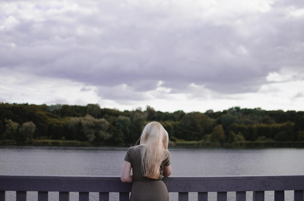 Foto mädchen mit langen blonden haaren in der natur, die gegen einen großen see stehen