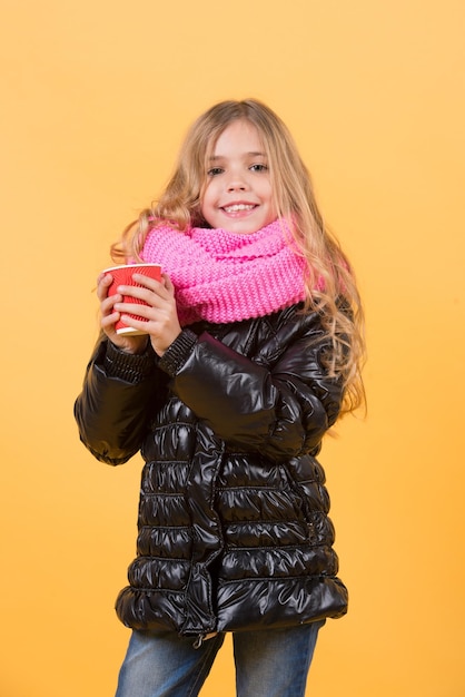 Mädchen mit langen blonden Haaren in schwarzer Jacke halten Tasse