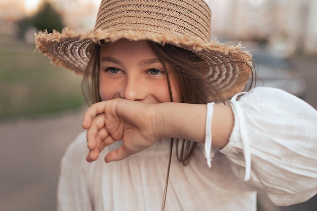 Mädchen mit langen Haaren und Sommersprossen in einem Strohhut lacht und bedeckt ihre Hand