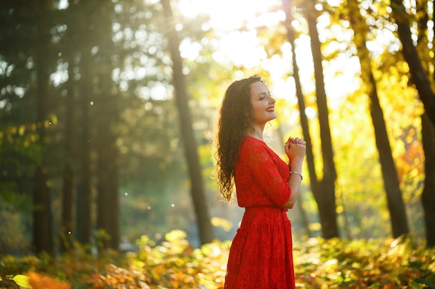 Mädchen mit Locken in einem roten Kleid im Herbstwald