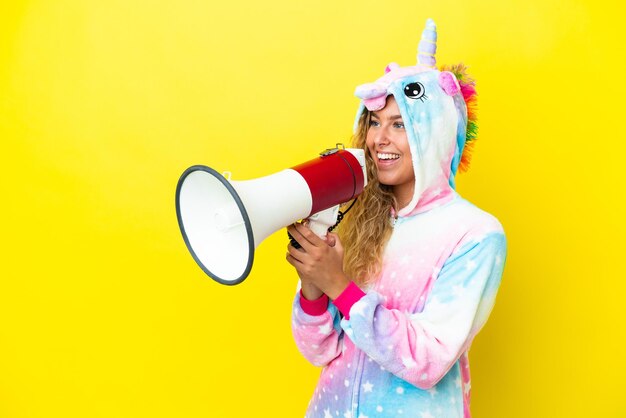 Foto mädchen mit lockigem haar, das einen einhornpyjama trägt, isoliert auf gelbem hintergrund, der durch ein megaphon schreit