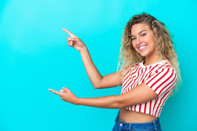 Foto mädchen mit lockigem haar isoliert auf blauem hintergrund, zeigt mit dem finger zur seite und präsentiert ein produkt