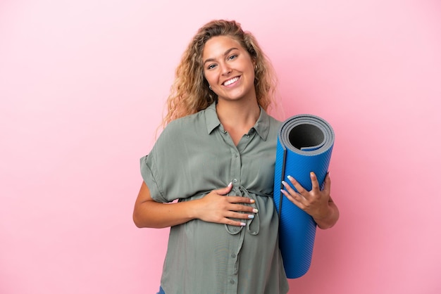 Foto mädchen mit lockigem haar isoliert auf rosa hintergrund schwanger und geht zu yoga-kursen