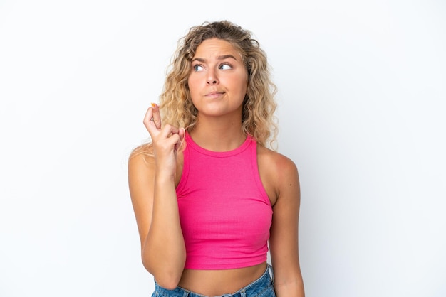 Mädchen mit lockigem Haar isoliert auf weißem Hintergrund mit gekreuzten Fingern und wünscht das Beste