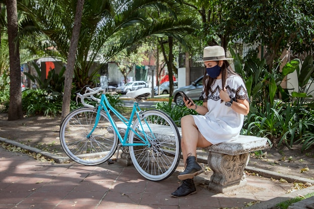 Mädchen mit Maske, die ihr Handy im Park überprüft