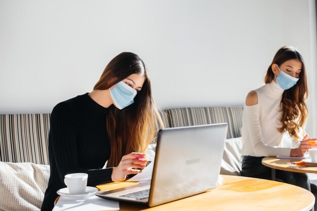 Mädchen mit Masken sitzen im Büro und arbeiten an einem Laptop.