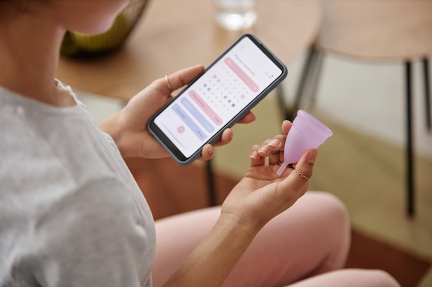 Mädchen mit Menstruationskuppe und Menstruations-Tracker-App