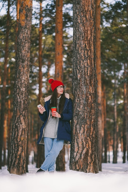 Mädchen mit Pappbecher und Telefon in einem verschneiten Wald