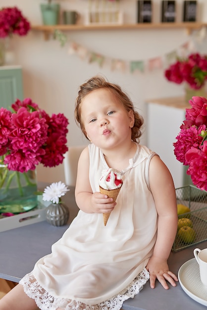 Mädchen mit Pfingstrosenstrauß und mit Eis. Strauß Pfingstrosen. Kind Mädchen mit Blumen. Kinderschutztag. Gefühle des Glücks und der Freude. Muttertag. Glückliche Kindheit