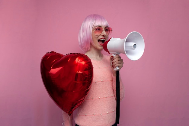 Mädchen mit rosa Haaren hält einen aufblasbaren Herzballon und schreit laut auf rosa Hintergrund