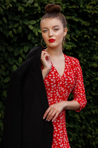 Mädchen mit roten Lippen, Abend Make-up in einem roten Kleid mit Druck und schwarzer Jacke, urbaner Kleidungsstil