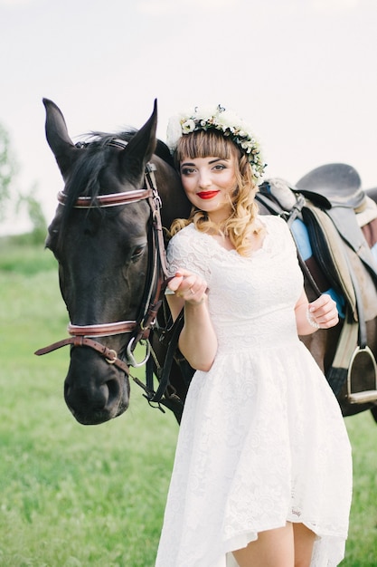 Mädchen mit roten Lippen in einem weißen Kleid neben einem schwarzen Pferd